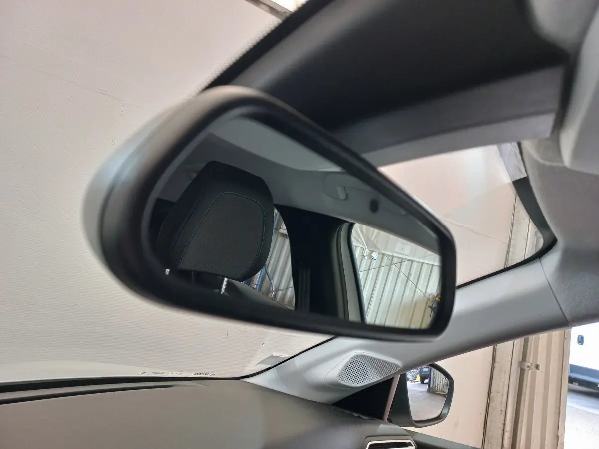 Rétroviseur intérieur gauche de la Peugeot 208 blanche, reflétant l'appui-tête et une porte de garage.