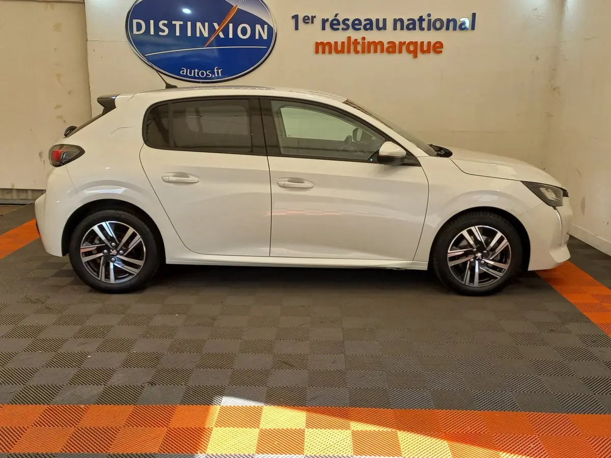 Profil côté gauche d'une Peugeot 208 blanche PureTech 100 S&S Allure 2021, avec jantes alliage et vitres teintées.