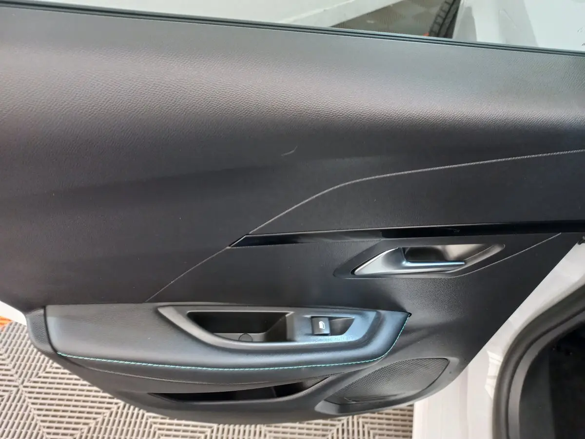 Gros plan sur la porte côté conducteur noire avec surpiqûres bleues d'une Peugeot 208 blanche 2021 PureTech Allure.