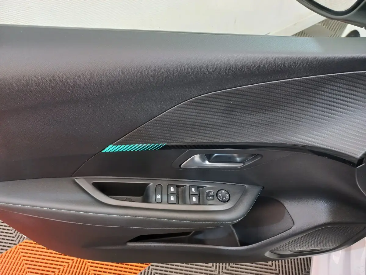 Vue rapprochée de la porte côté gauche d'une Peugeot 208 blanche, avec commandes de vitres et poignée argentée.