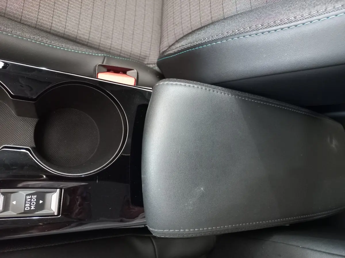 Gros plan sur l'accoudoir noir et le porte-gobelet central de la Peugeot 208 PureTech 100 S&S Allure blanche.