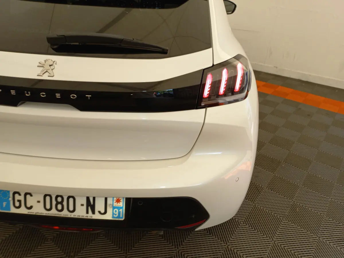 Vue arrière droite d'une Peugeot 208 blanche avec feux arrière LED allumés dans un garage.