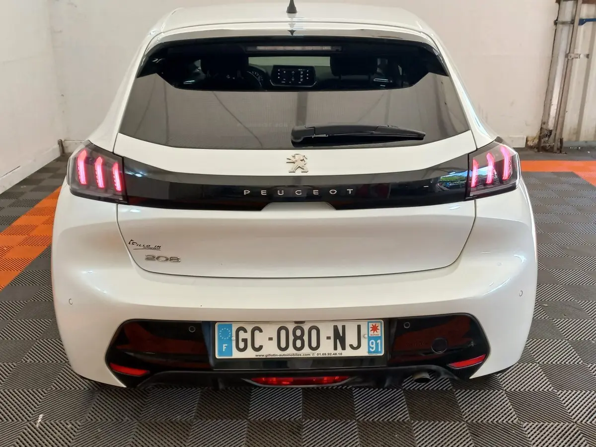 Vue arrière d'une Peugeot 208 blanche avec feux LED allumés et logo Peugeot visible sur le hayon.
