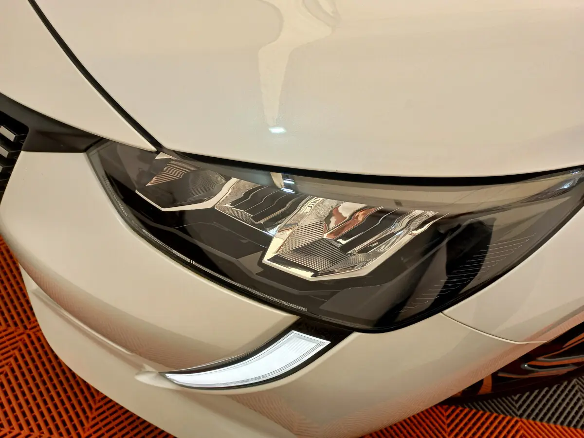 Gros plan sur le phare avant droit blanc d'une Peugeot 208 PureTech 100 S&S Allure 2021, détails LED visibles.