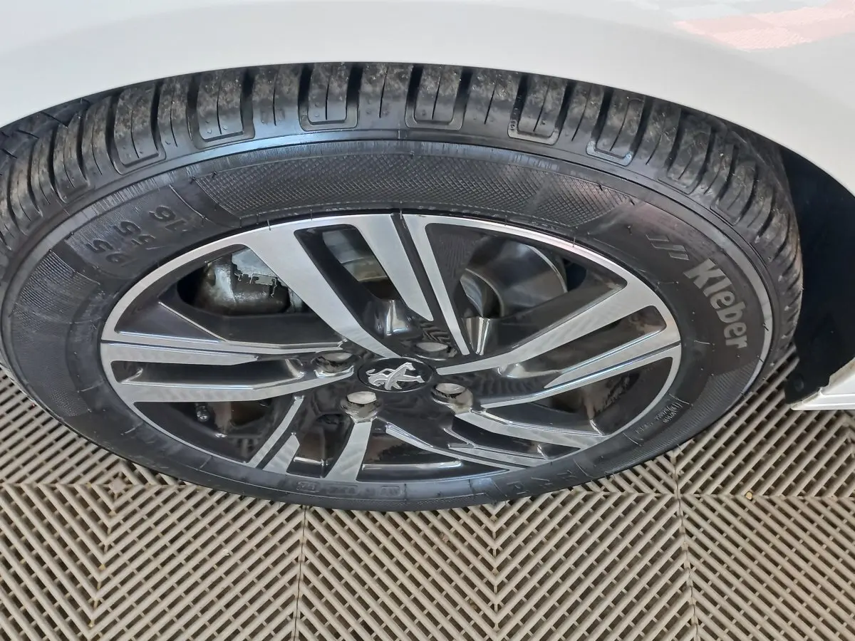 Gros plan sur la roue avant droite d'une Peugeot 208 blanche avec jante alliage au design moderne.