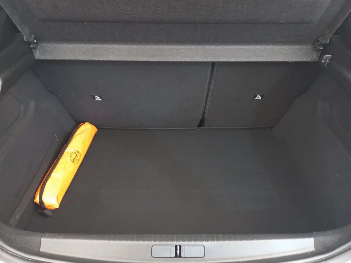 Coffre ouvert d'une Peugeot 208 blanc, vue plongeante montrant un rangement noir avec un sac orange sur la gauche.