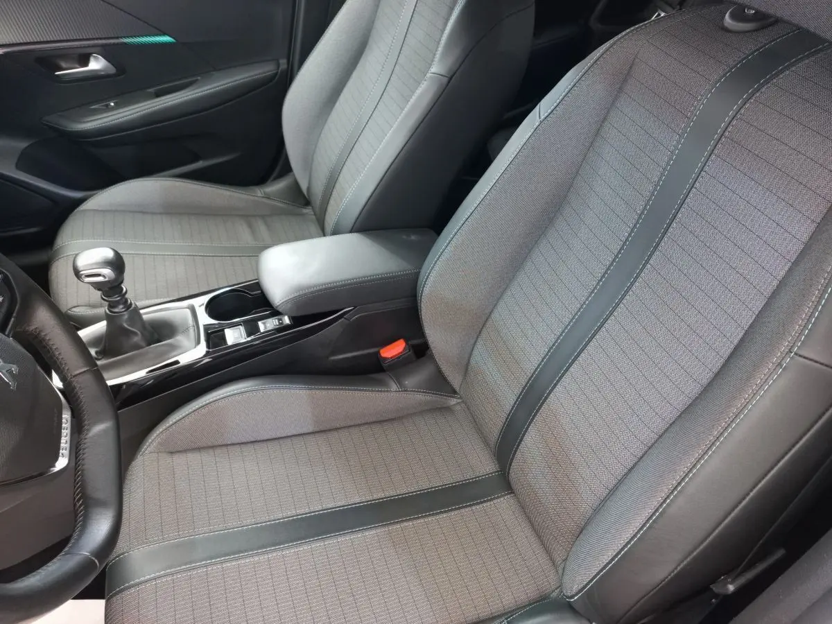 Vue intérieure rapprochée des sièges avant gris et noir d'une Peugeot 208 PureTech 100 S&S Allure 2021 avec levier de vitesse manuel.