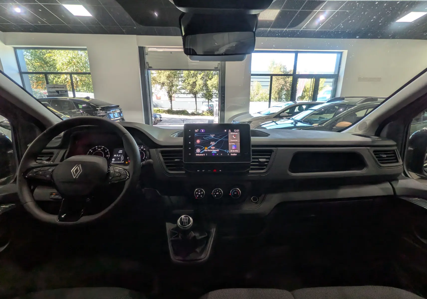 Vue intérieure frontale du Renault Trafic Combi 2025, tableau de bord noir avec écran tactile et volant multifonction.