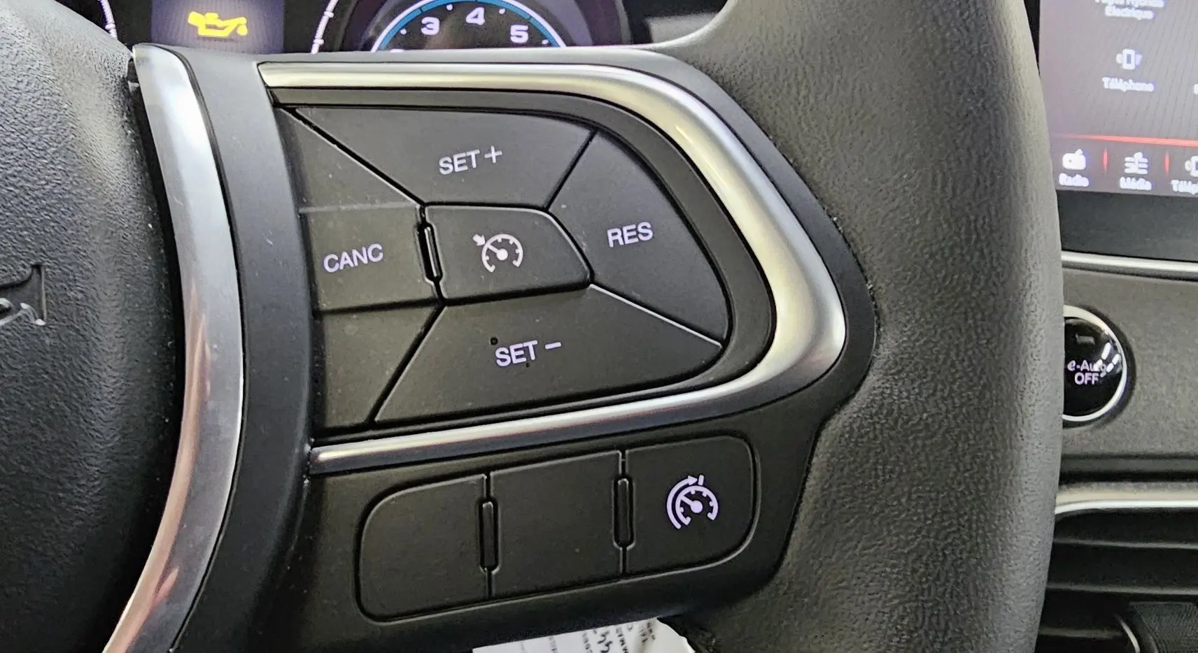 Gros plan sur les commandes de régulateur de vitesse au volant d'une FIAT 500X hybride 2024, intérieur noir.