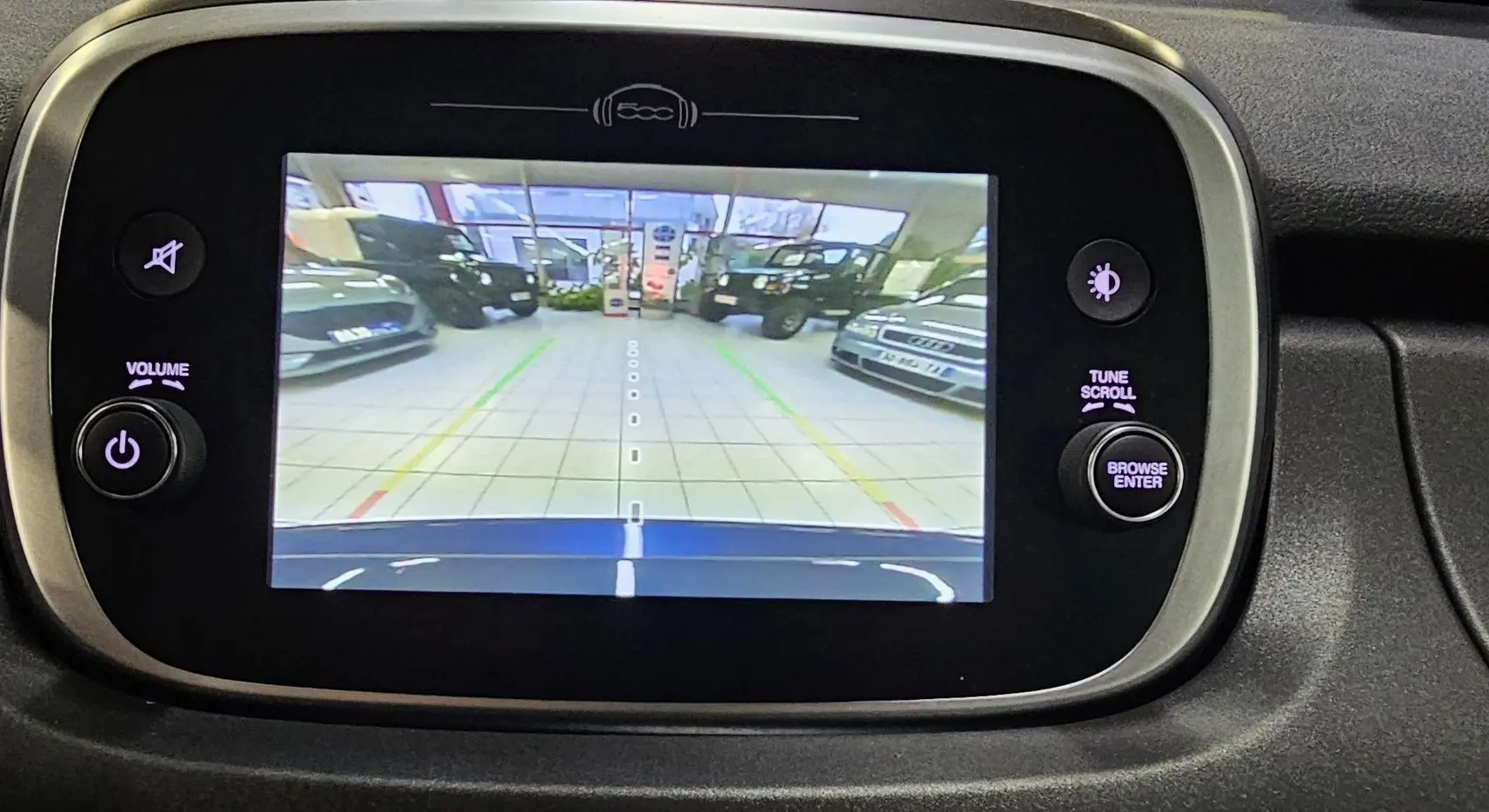 Écran central de la FIAT 500X 2024 montrant la caméra de recul avec vue sur le capot bleu et le garage en arrière-plan.