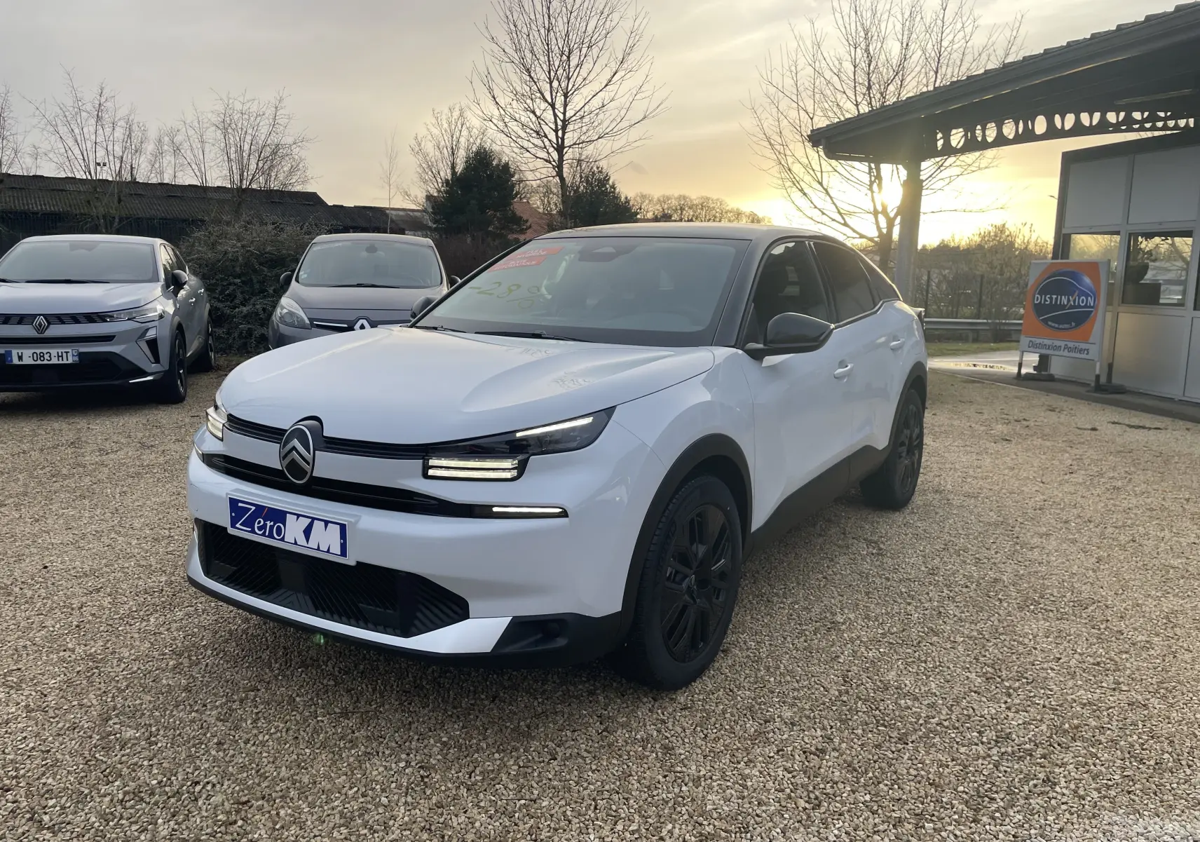 Citroën C4 hybride blanc Okenite avec toit noir Perla, vue 3/4 avant droit sur parking extérieur au coucher du soleil.