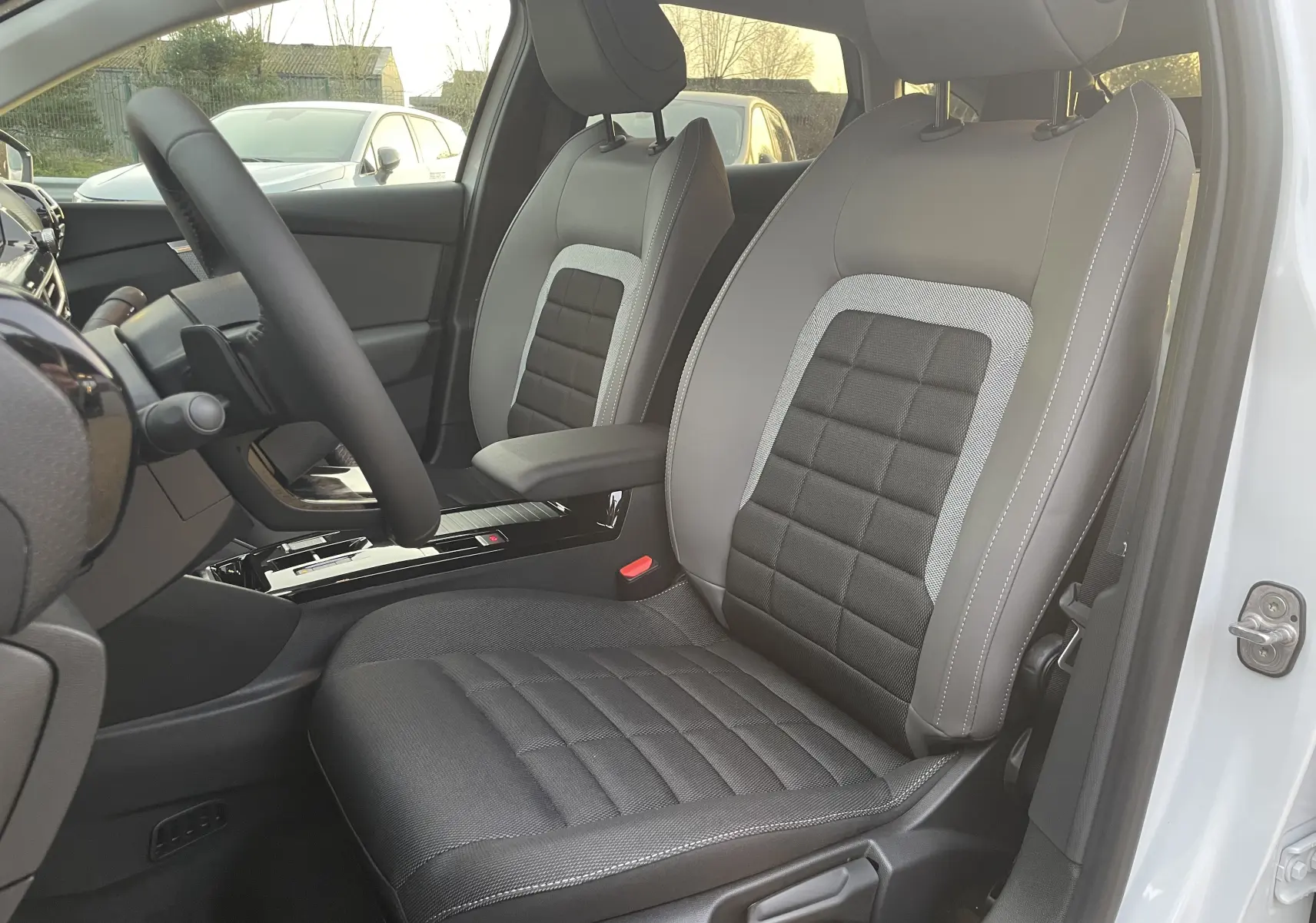 Vue intérieure côté conducteur de la Citroën C4 hybride 2025, sièges tissu noir et gris, volant et console centrale visibles.