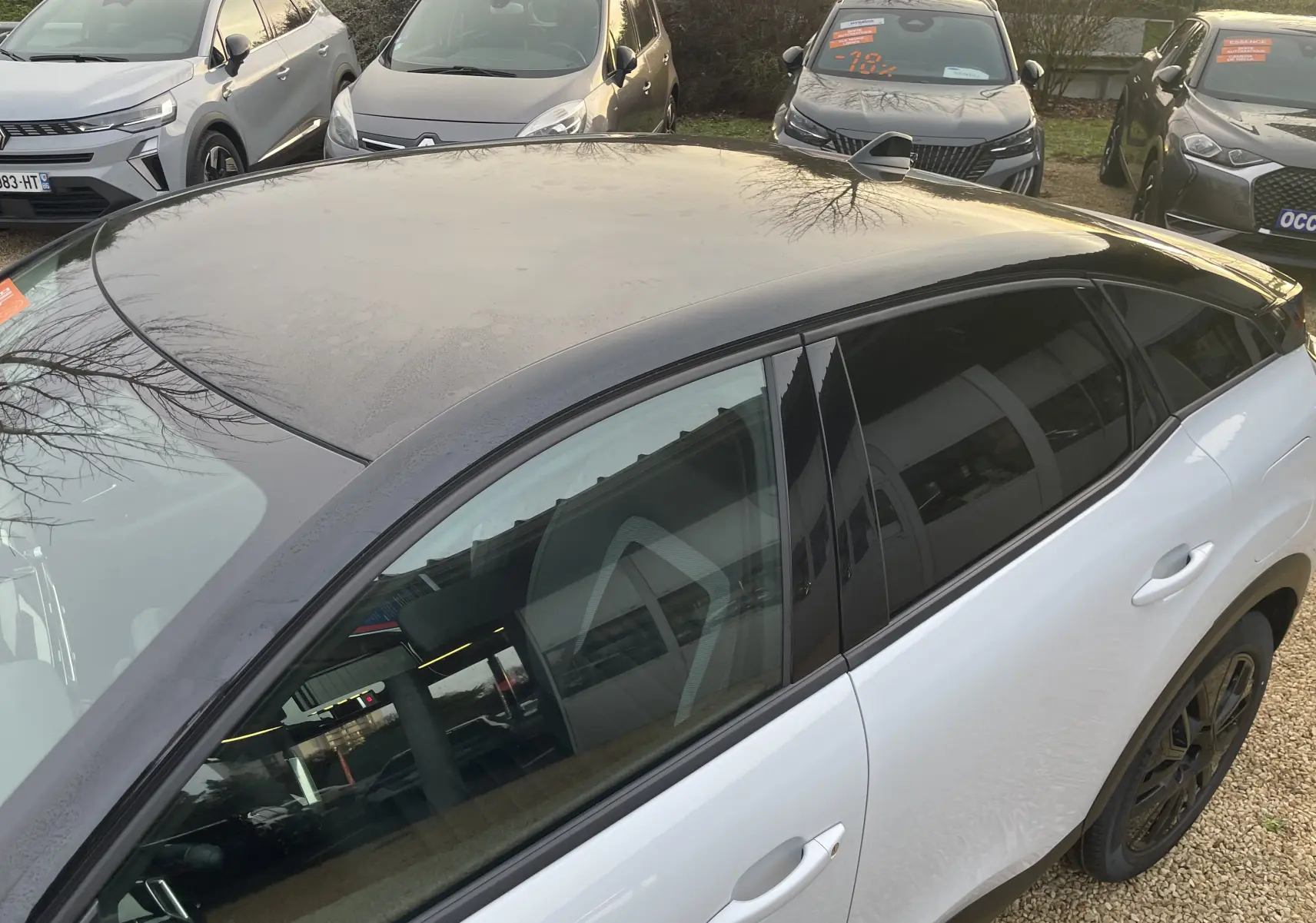 Vue 3/4 arrière côté droit de la Citroën C4 blanche Okenite avec toit noir Perla et jantes noires, en extérieur.
