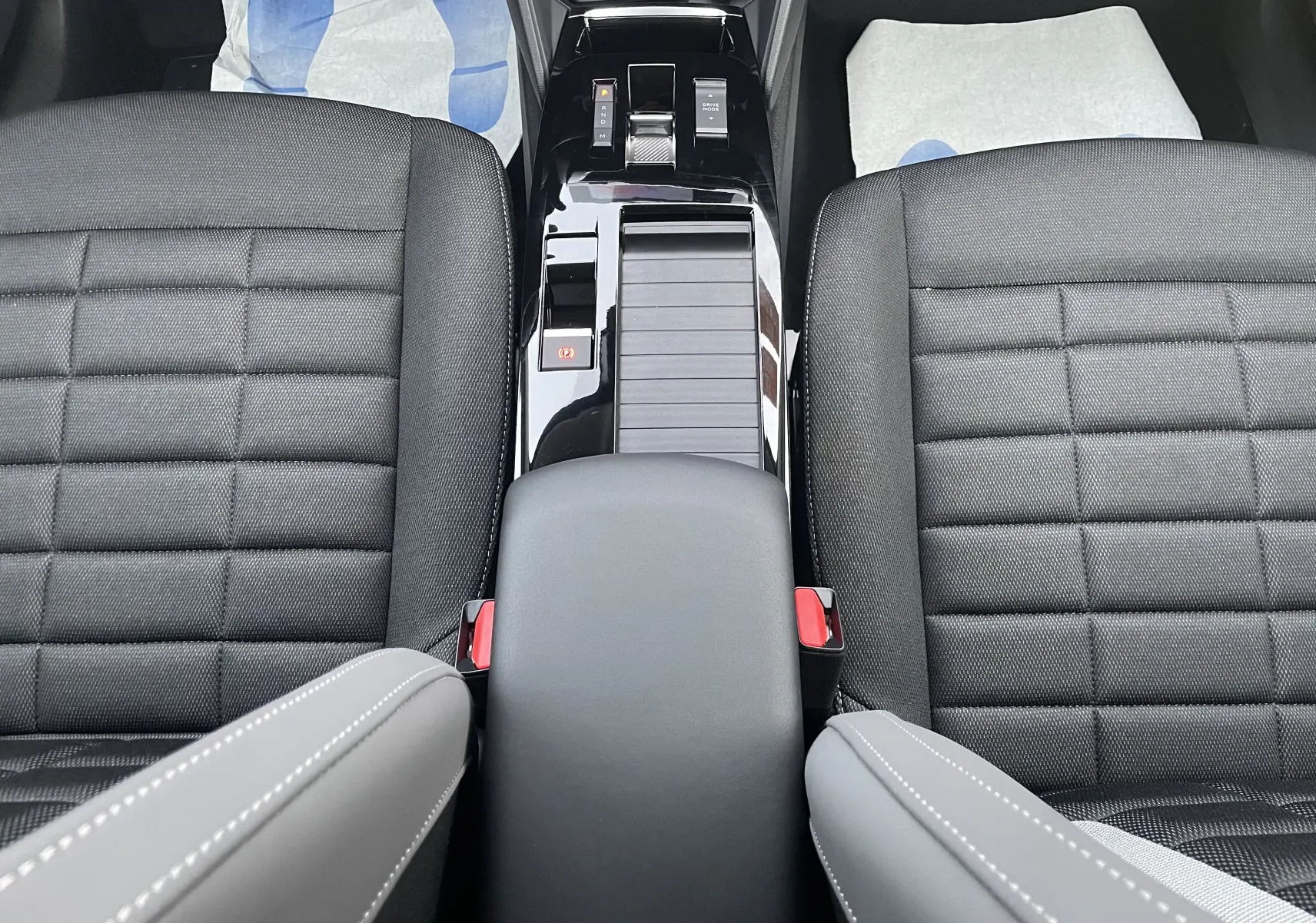 Vue plongeante sur la console centrale noire brillante et les sièges avant en tissu noir de la Citroën C4 hybride 2025.