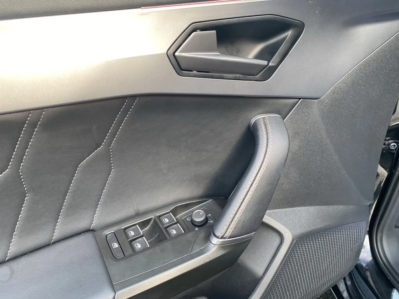 Détail de la porte avant gauche noire de la CUPRA Leon 2023 avec commandes des vitres et poignée en cuir.