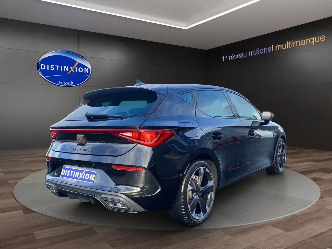 Vue 3/4 arrière droite d'une CUPRA Leon noire 2023 avec jantes alliage et feux arrière LED allumés.