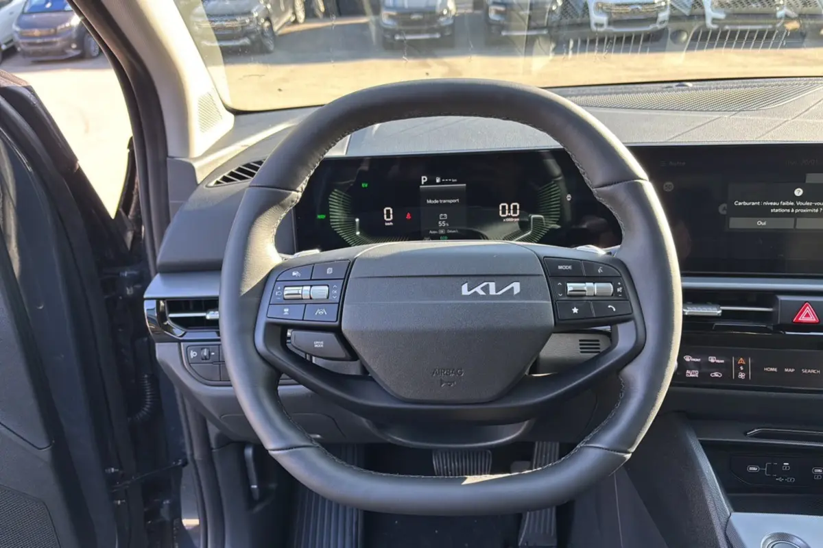 Vue intérieure centrée sur le volant cuir multifonctions du Kia Sportage gris eclipse, tableau de bord numérique visible.
