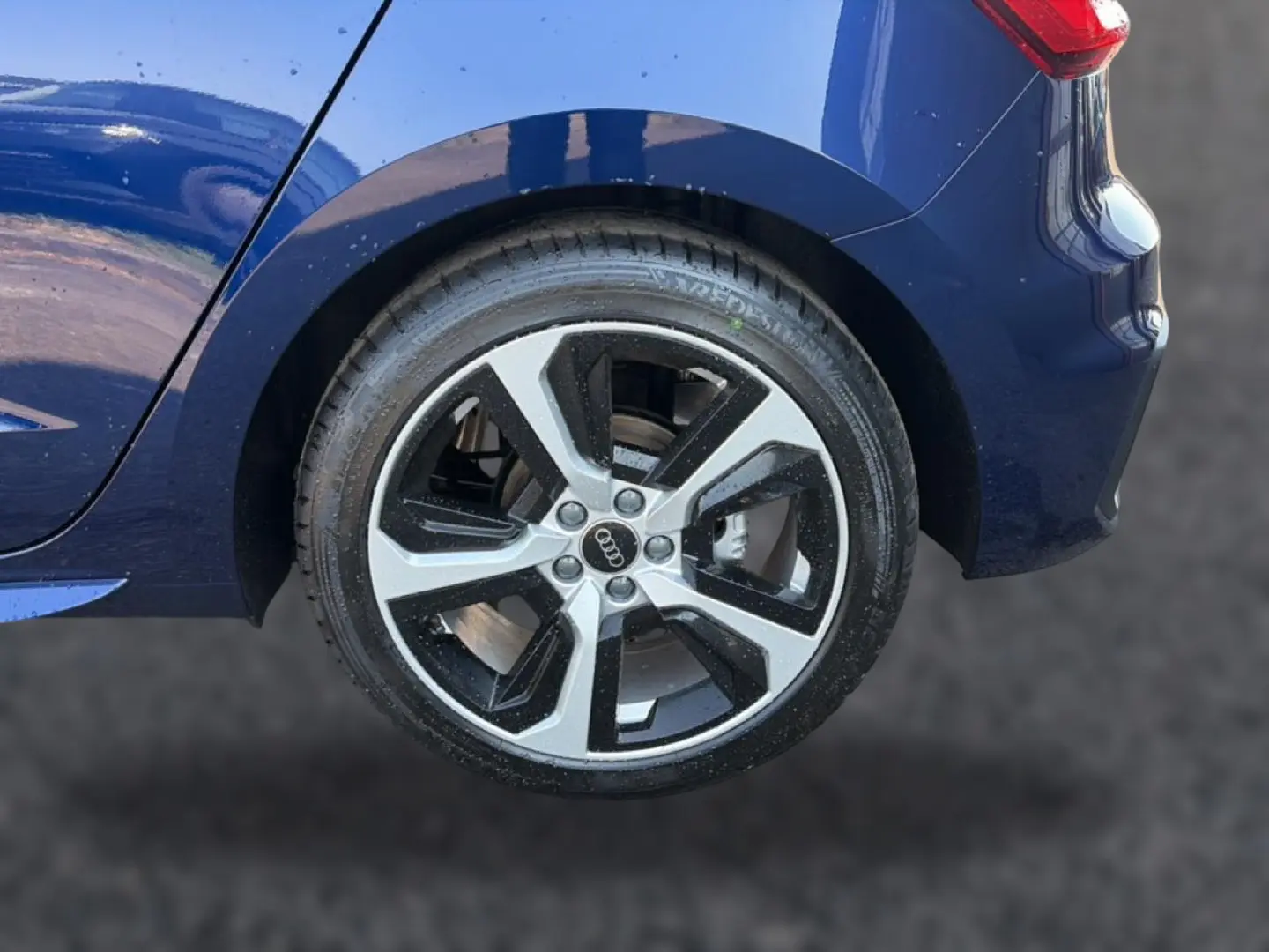 Gros plan sur la roue arrière droite d’une Audi A1 Sportback bleu foncé avec jante alu bicolore et partie arrière du véhicule visible.
