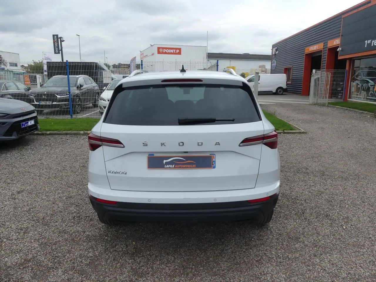 Vue arrière d'un SUV SKODA KAROQ blanc avec feux arrière LED et logo ŠKODA visible sur un parking.
