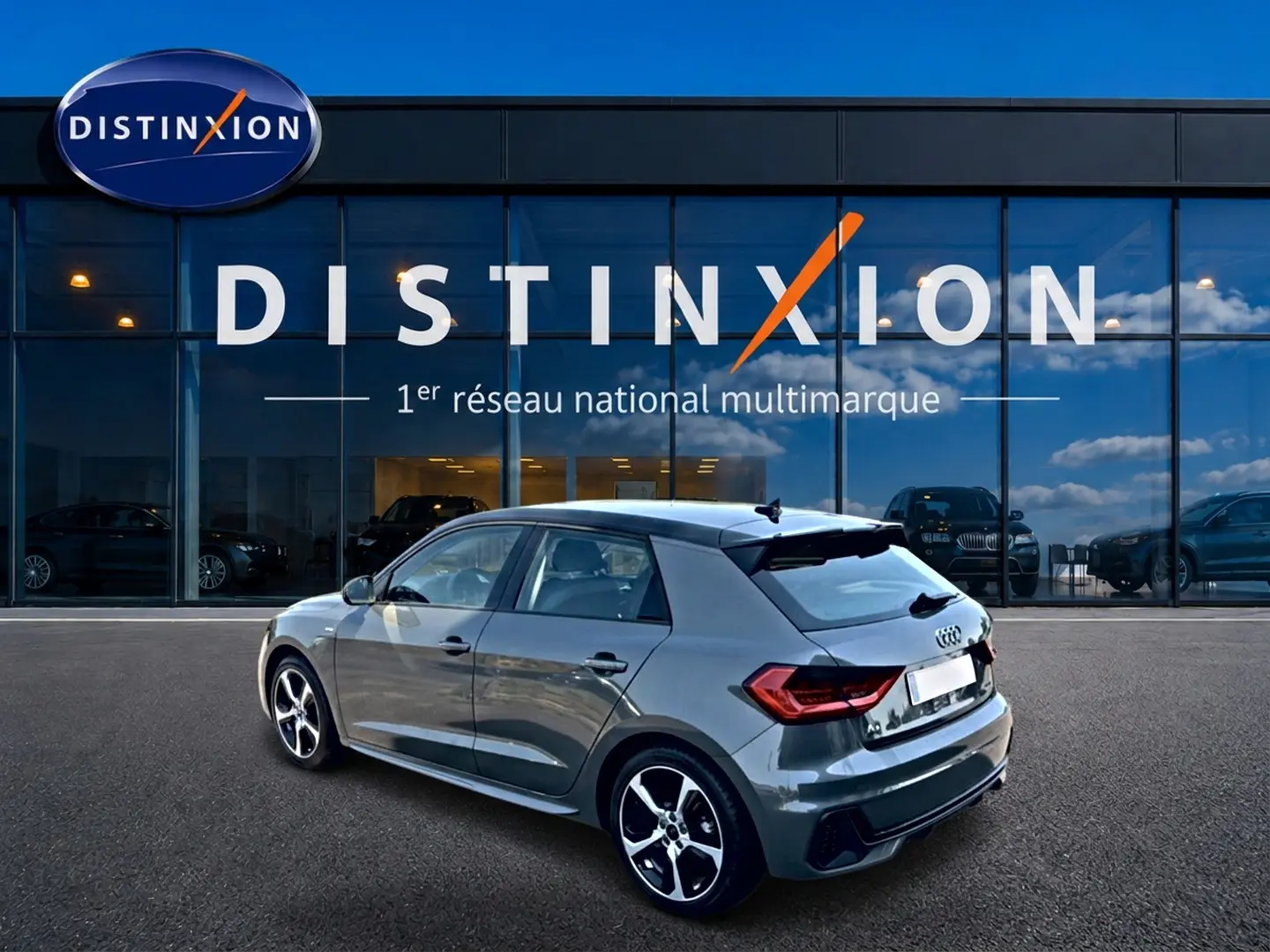 Audi A1 Sportback gris chronos vue 3/4 arrière droit avec jantes alu et becquet noir devant une vitrine Distinxion.