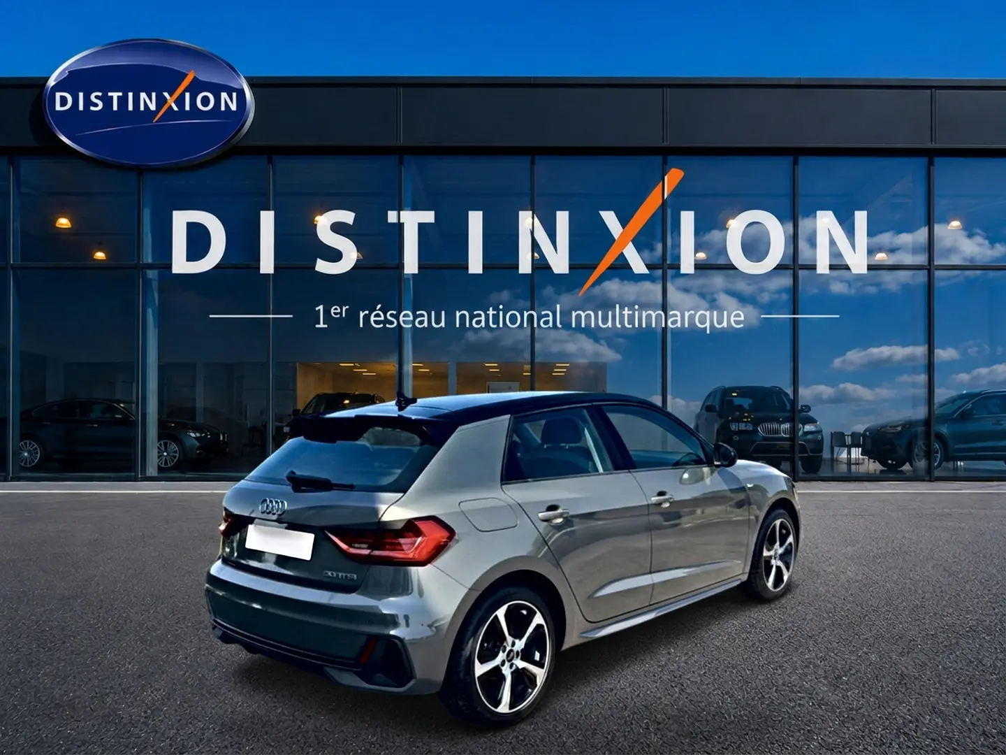 Audi A1 Sportback gris chronos avec toit noir, vue 3/4 arrière droit, stationnée devant une vitrine Distinxion.