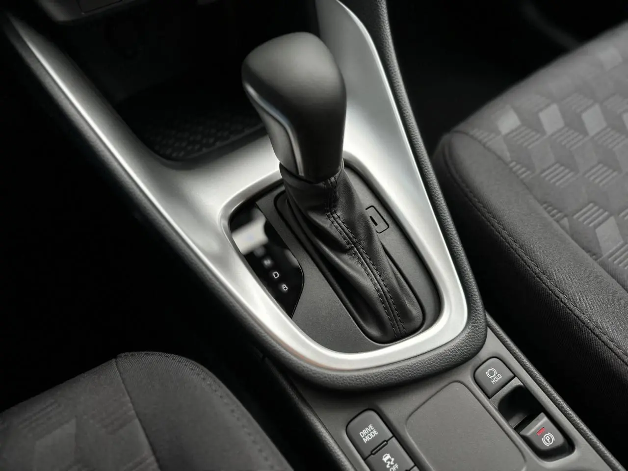 Gros plan sur la console centrale de la Toyota Yaris hybride 2025, avec levier de boîte auto et sellerie tissu noir.