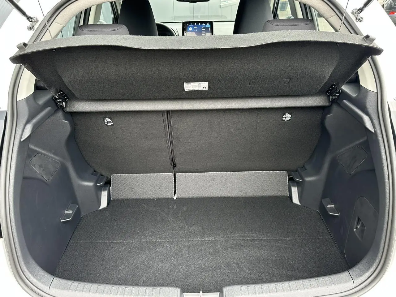 Coffre ouvert d'une Toyota Yaris blanche 2025, vue arrière montrant le double plancher et la banquette arrière noire.