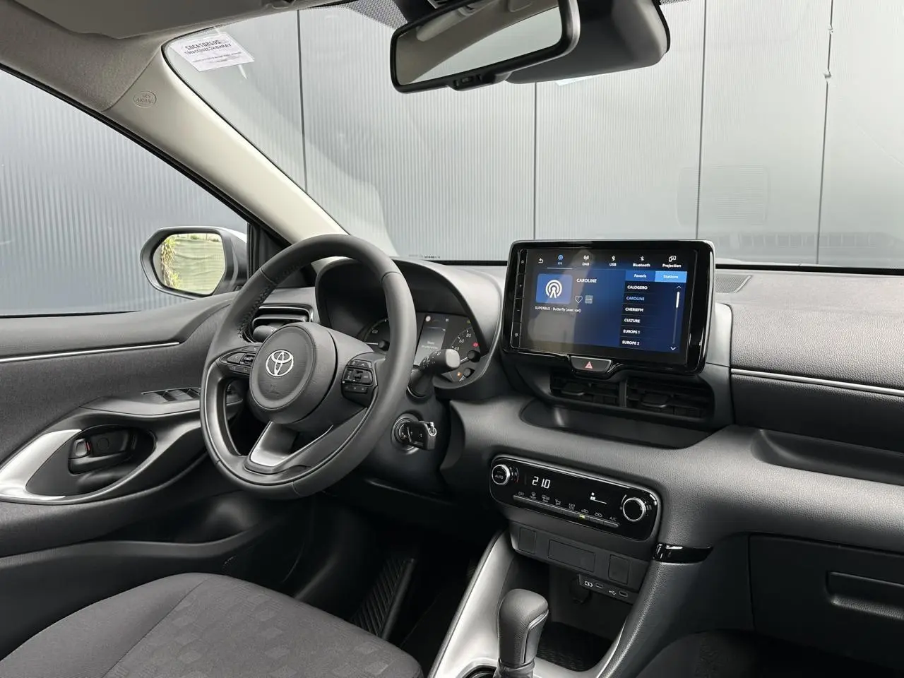 Intérieur avant gauche de la Toyota Yaris hybride 2025 avec volant multifonction cuir et écran tactile 9 pouces allumé.