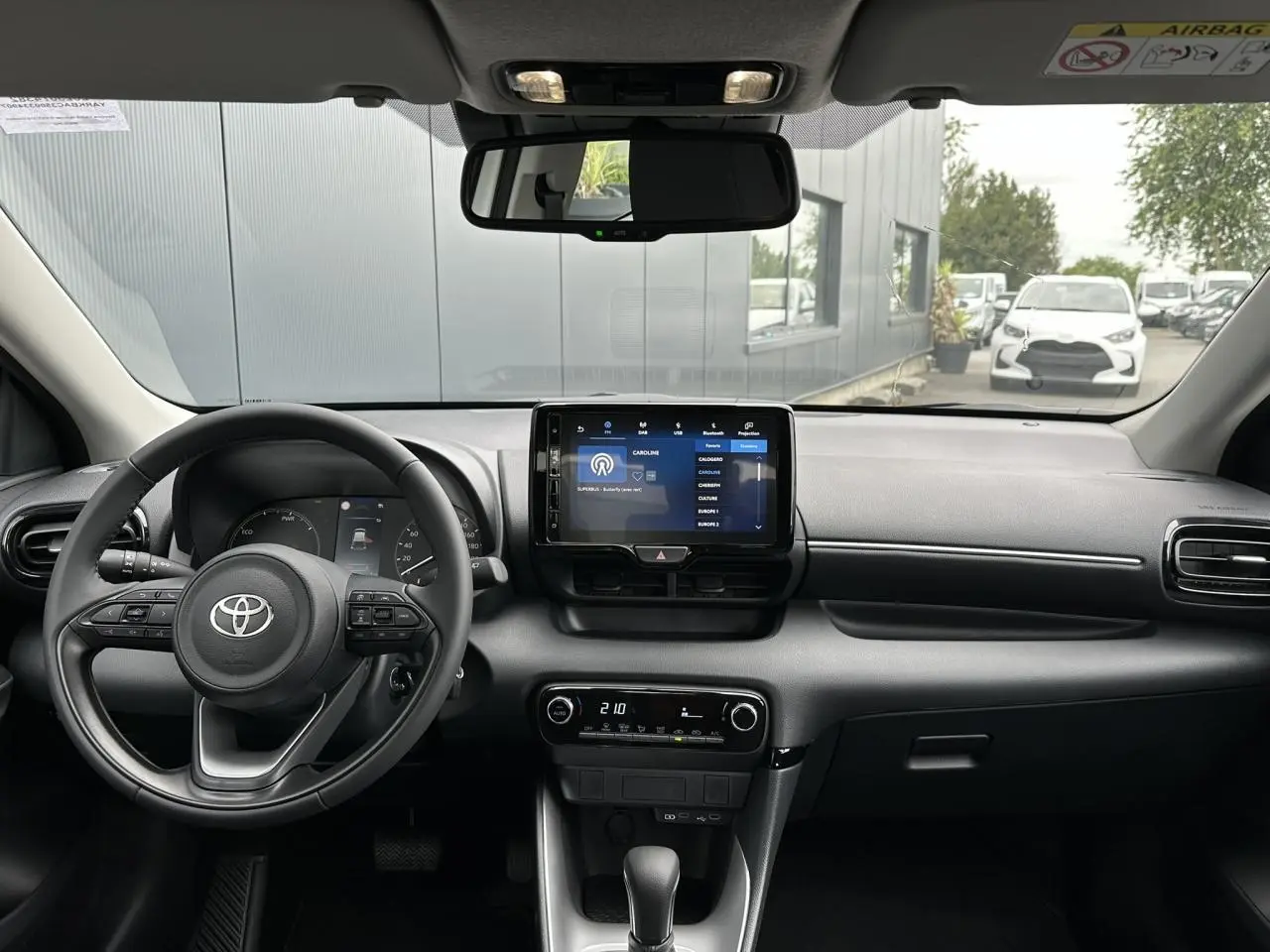 Vue intérieure avant de la Toyota Yaris hybride 2025, tableau de bord noir avec écran tactile central et volant multifonction cuir.