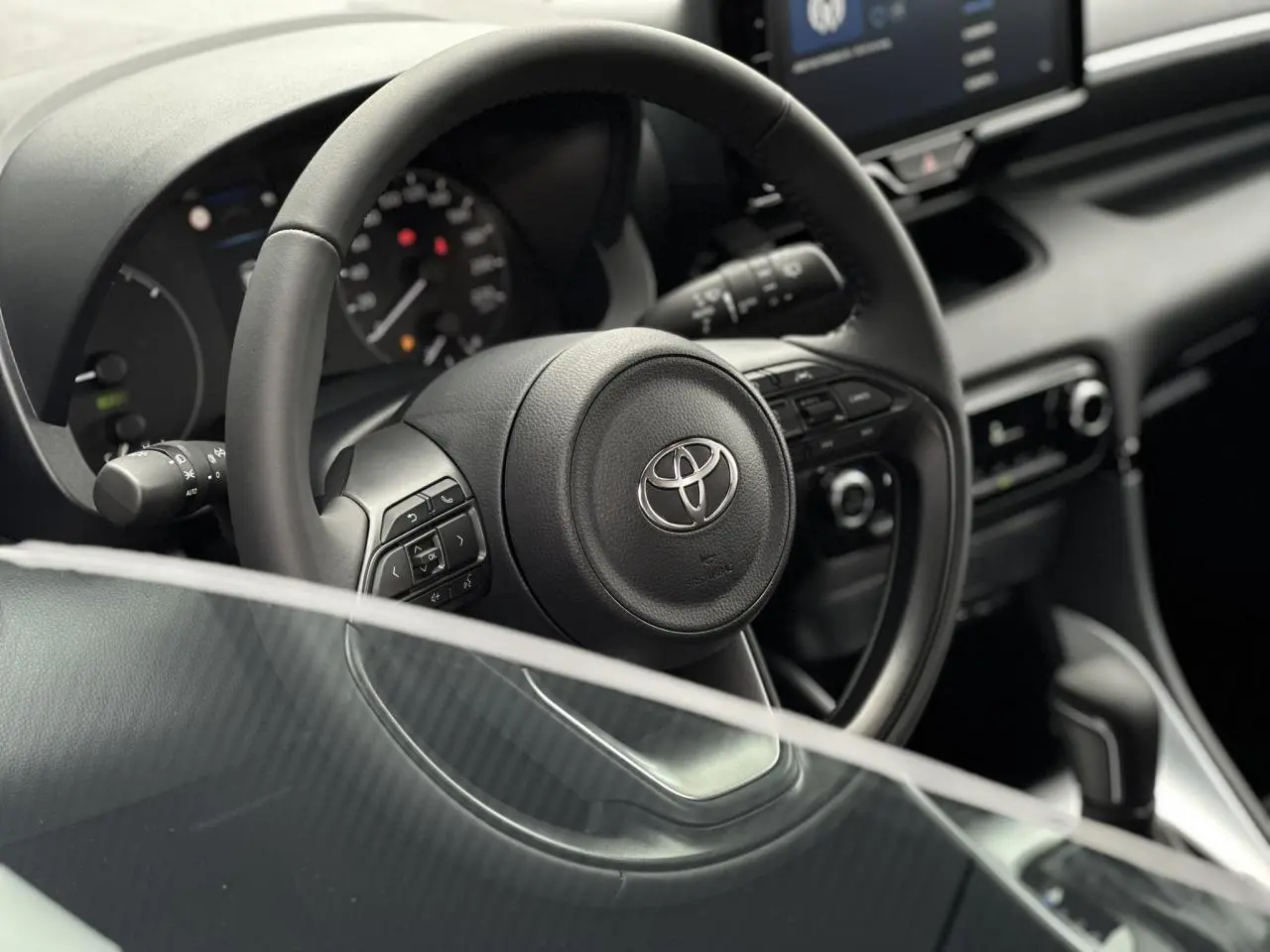 Vue rapprochée du volant en cuir noir d'une Toyota Yaris hybride 2025, avec commandes multifonctions visibles.