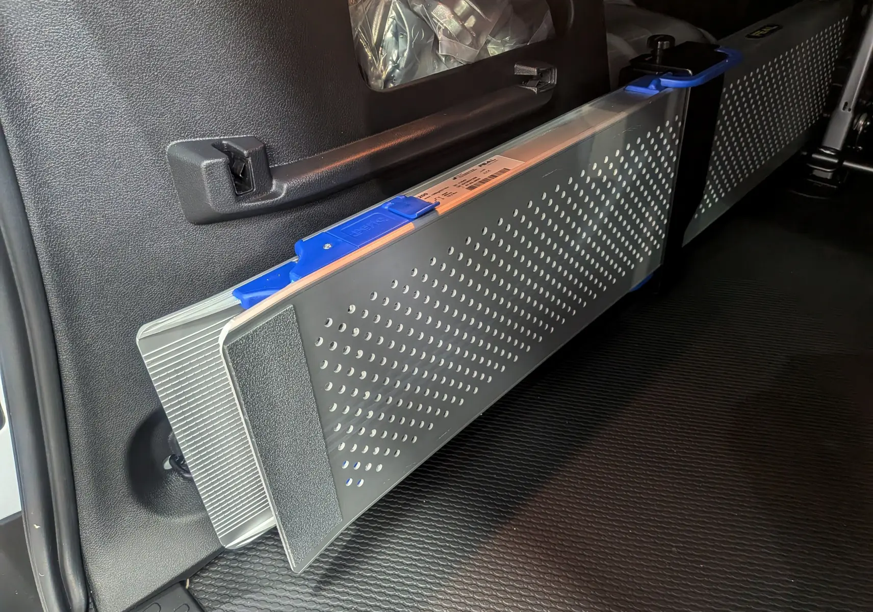 Détail intérieur montrant une rampe pliante grise avec poignée bleue dans un Renault Trafic Combi blanc.