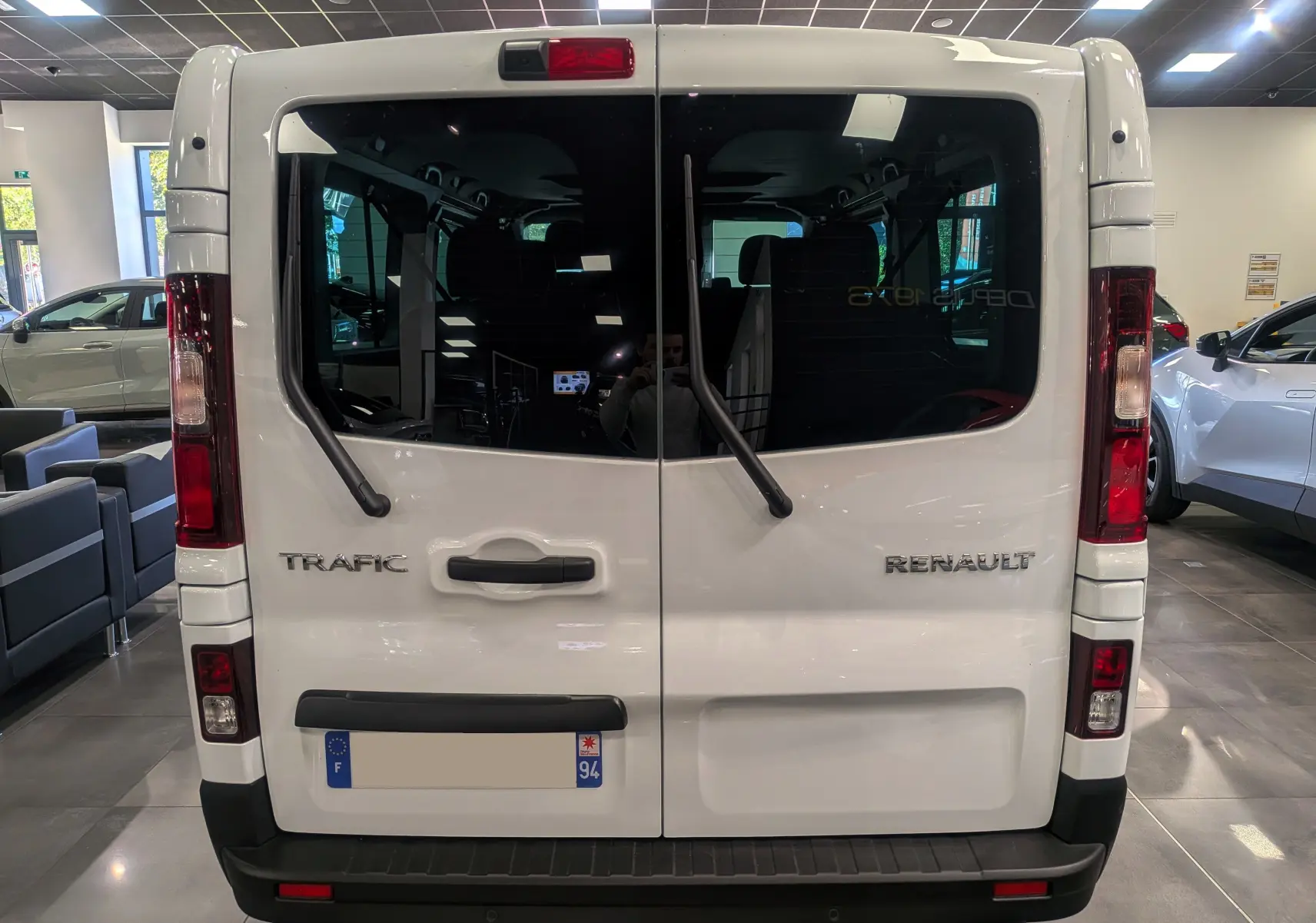 Vue arrière du Renault Trafic Combi blanc Glacier avec portes vitrées et essuie-glaces verticaux en showroom.