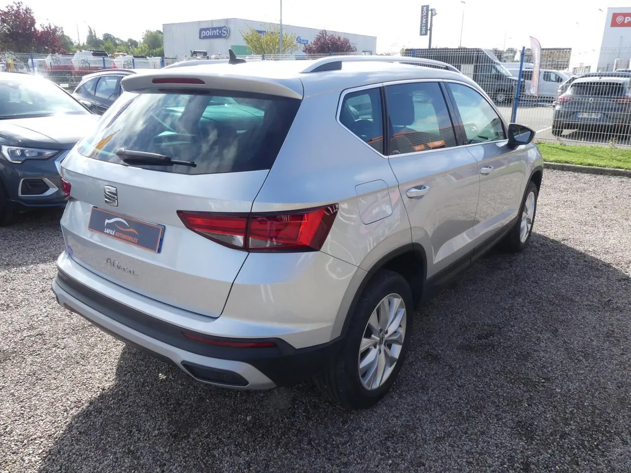 Vue 3/4 arrière droite d'un SEAT Ateca gris clair avec jantes alliage 17'' et barres de toit chromées.