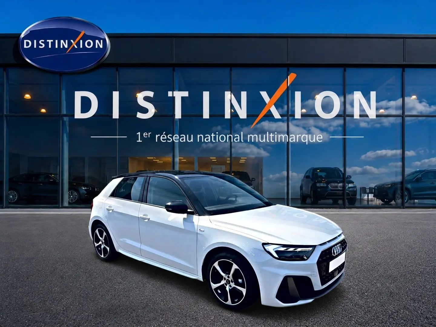 Audi A1 Sportback blanc à toit noir en 3/4 avant droit, avec jantes alu et calandre S line visible devant un showroom.