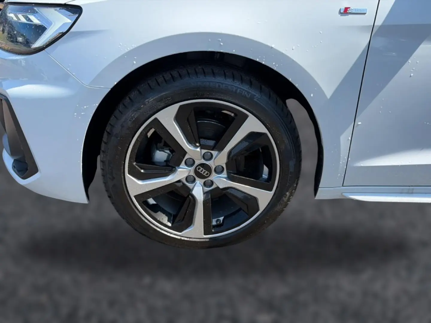 Gros plan sur la roue avant droite et l'aile blanche d'une Audi A1 Sportback 30 TFSI S line 2026 avec jante alu bicolore.