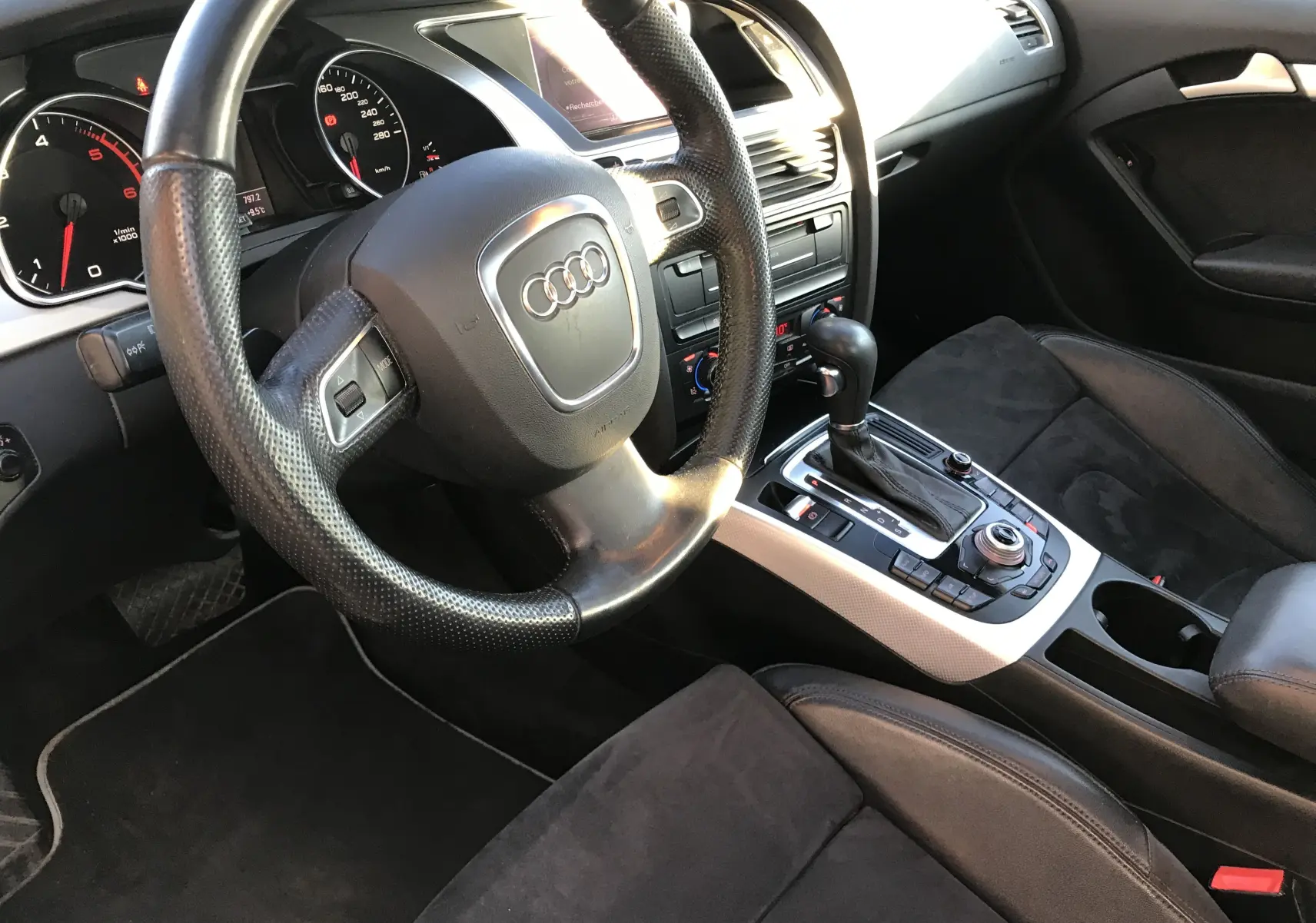 Intérieur noir de l'Audi A5 2012, vue côté conducteur sur le volant, tableau de bord et console centrale avec boîte auto.