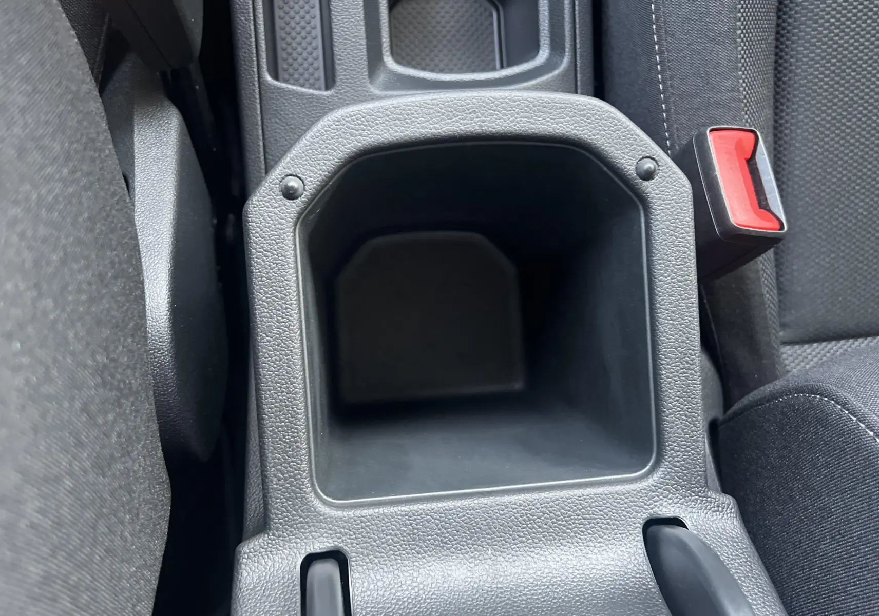 Gros plan sur le rangement central noir entre les sièges avant du Volkswagen T-Roc 2024 gris Indium.