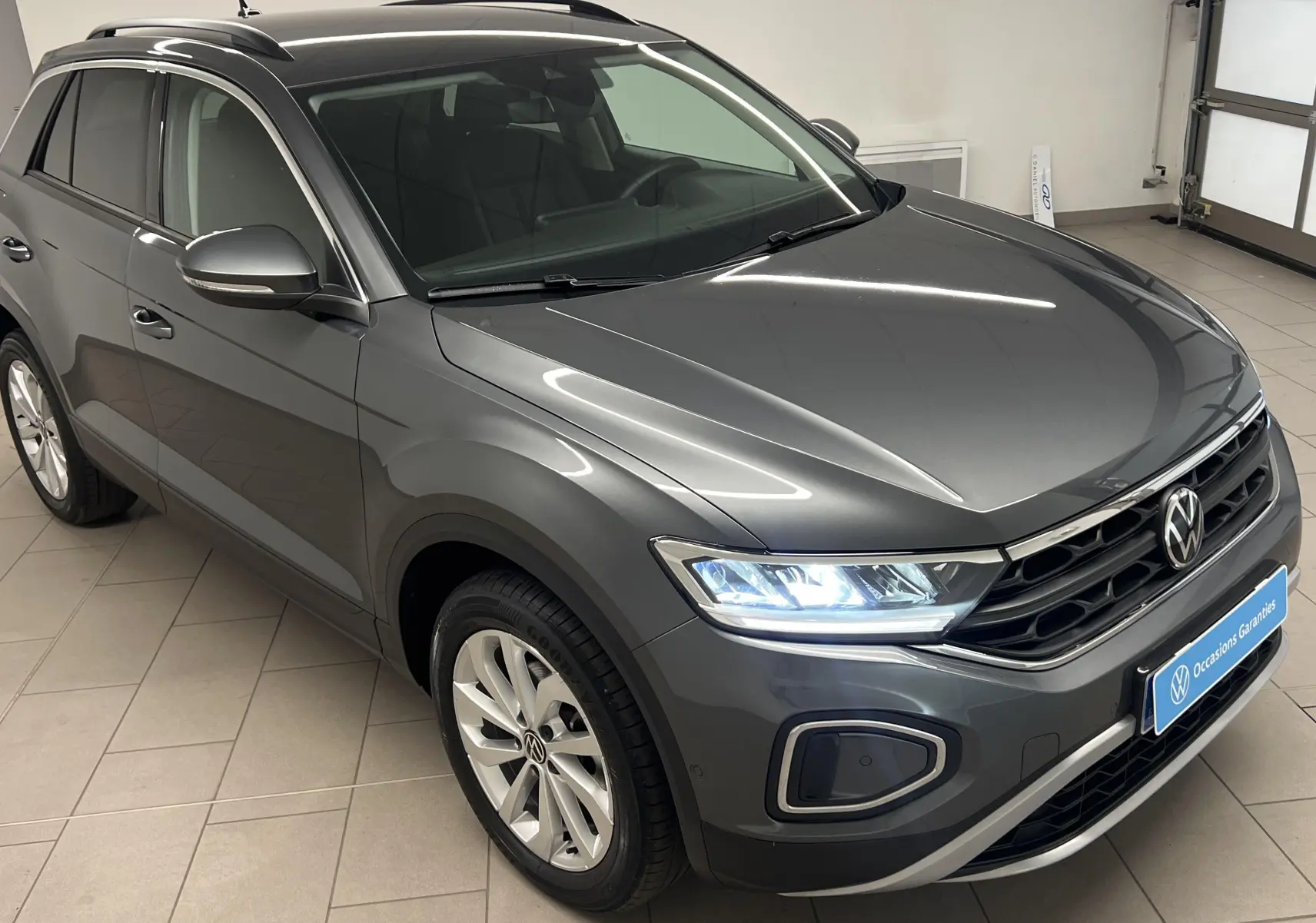 Volkswagen T-Roc gris Indium vu en 3/4 avant droit avec jantes alliage 17'' Johannesburg et phares allumés.