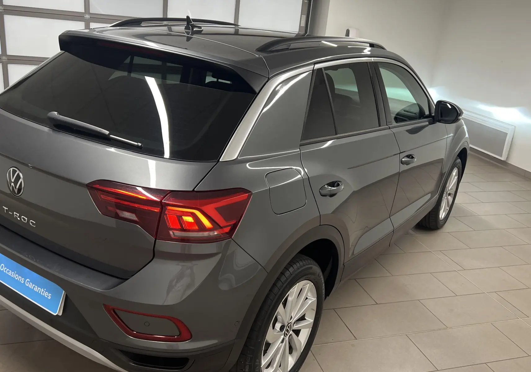 Volkswagen T-Roc gris Indium vu en 3/4 arrière droit, avec jantes alliage 17'' Johannesburg et feux allumés.
