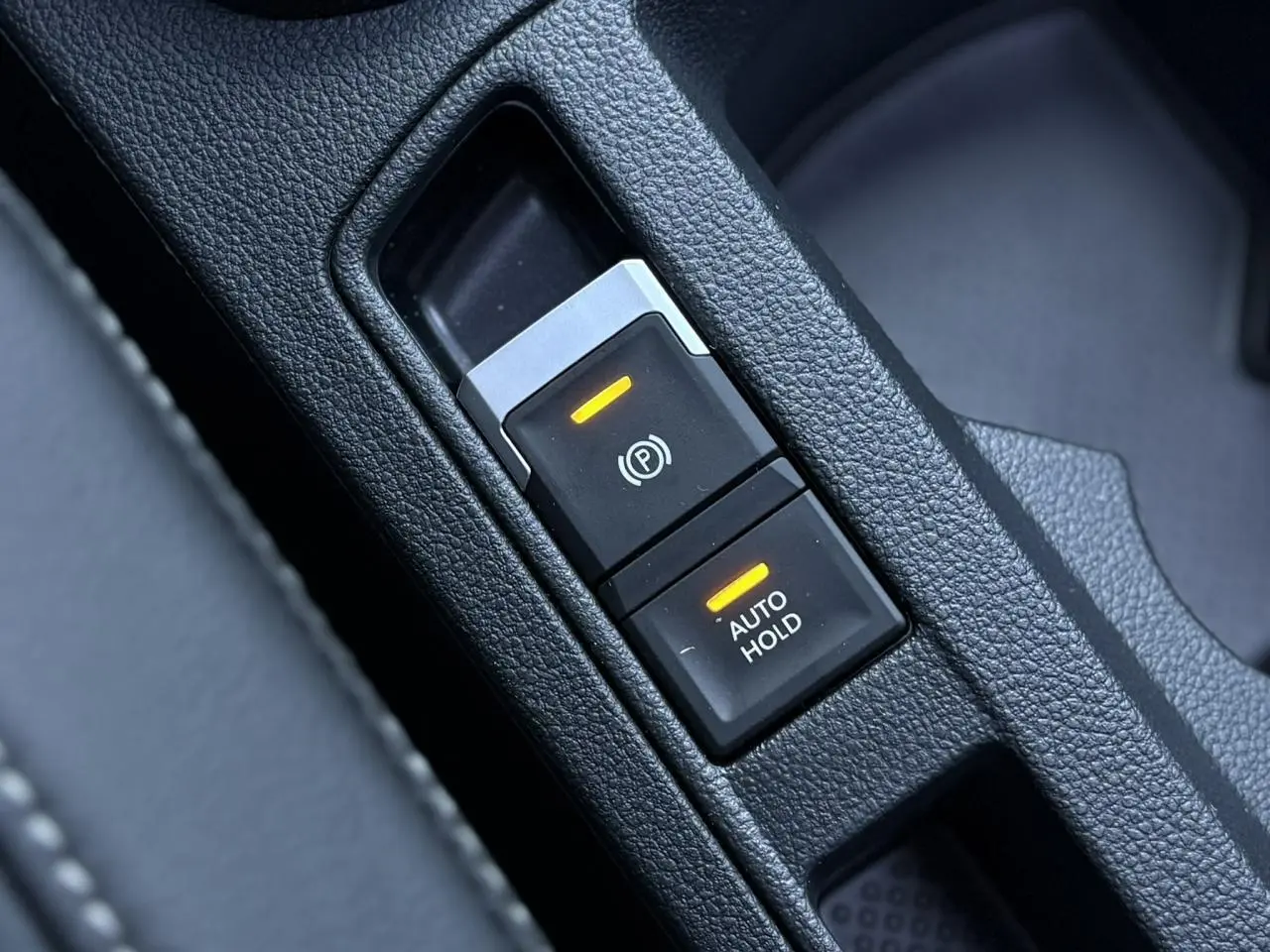 Gros plan sur les commandes du frein de stationnement électromécanique et Auto Hold du Volkswagen T-Roc gris pyrite 2025.