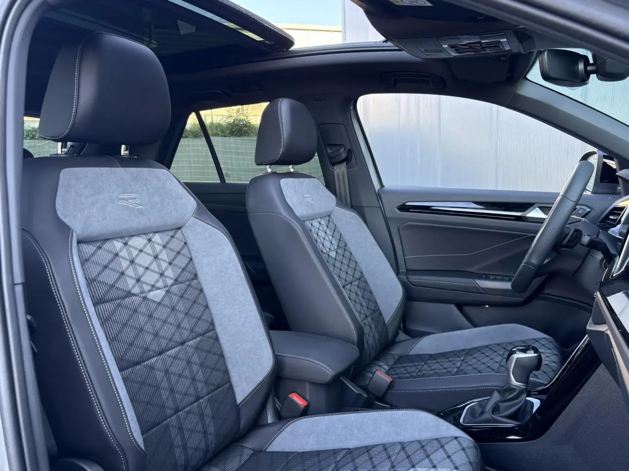 Intérieur du Volkswagen T-Roc 2025 vu côté droit, sièges R-Line en cuir et tissu gris avec toit ouvrant panoramique.