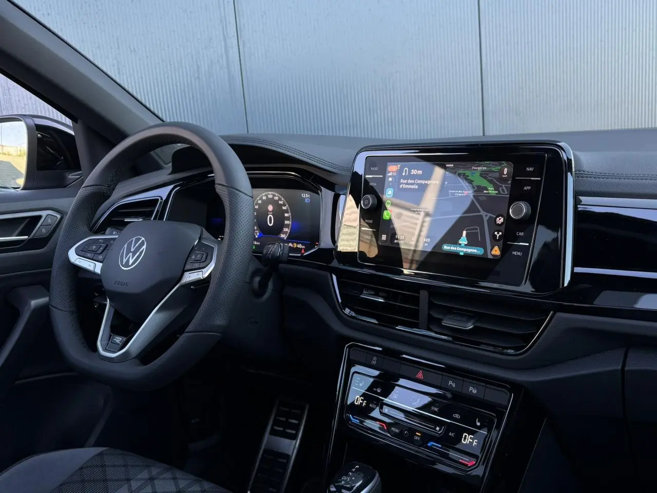 Intérieur du Volkswagen T-Roc 2025, vue du poste de conduite avec volant cuir R-Line et écran tactile central affichant la navigation.