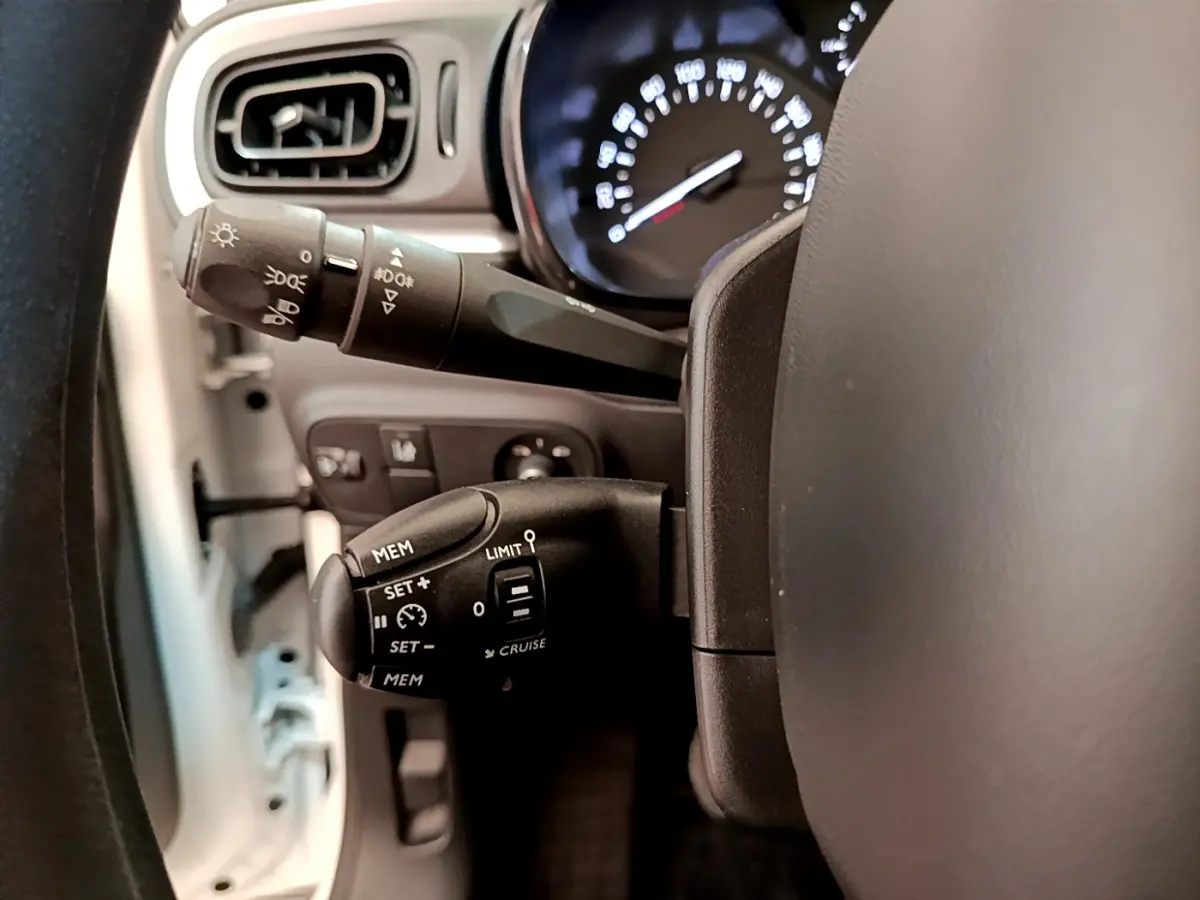 Gros plan sur les commandes de régulateur et feux au volant d'une Citroën C3 blanche, tableau de bord en arrière-plan.