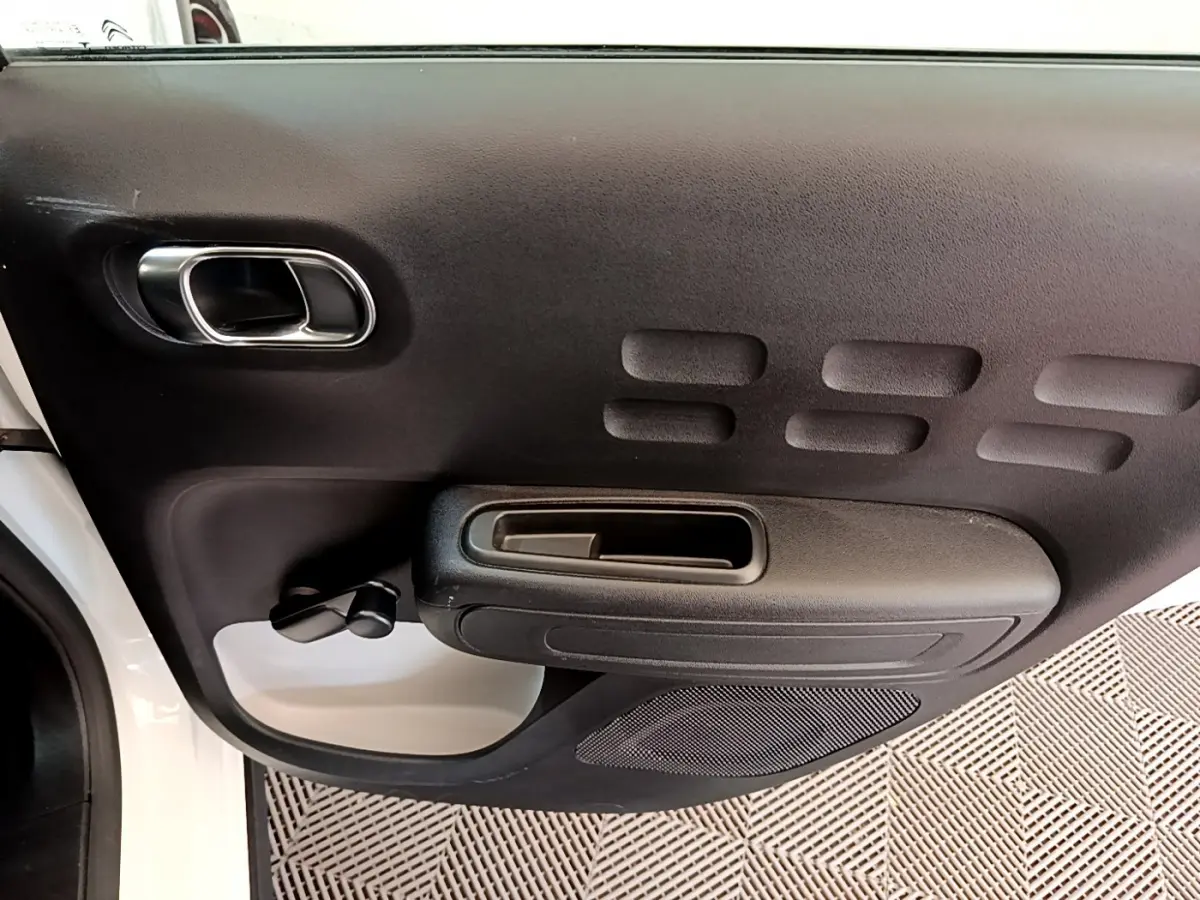 Intérieur côté gauche de la porte avant d'une Citroën C3 blanche 2019, avec poignée et commande de vitre manuelle.