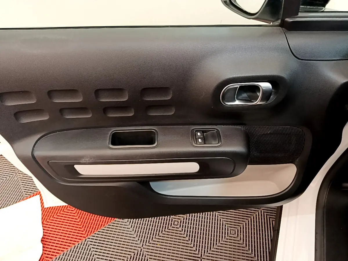 Gros plan sur la porte côté droit de la Citroën C3 blanche, montrant la poignée intérieure et les commandes des vitres.