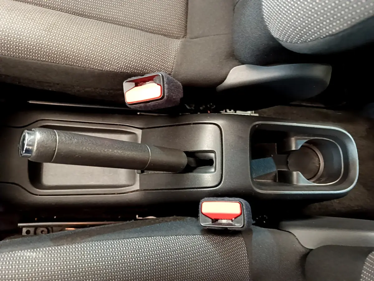 Vue plongeante sur la console centrale noire de la Citroën C3 PureTech 82, avec frein à main et ceintures rouges.