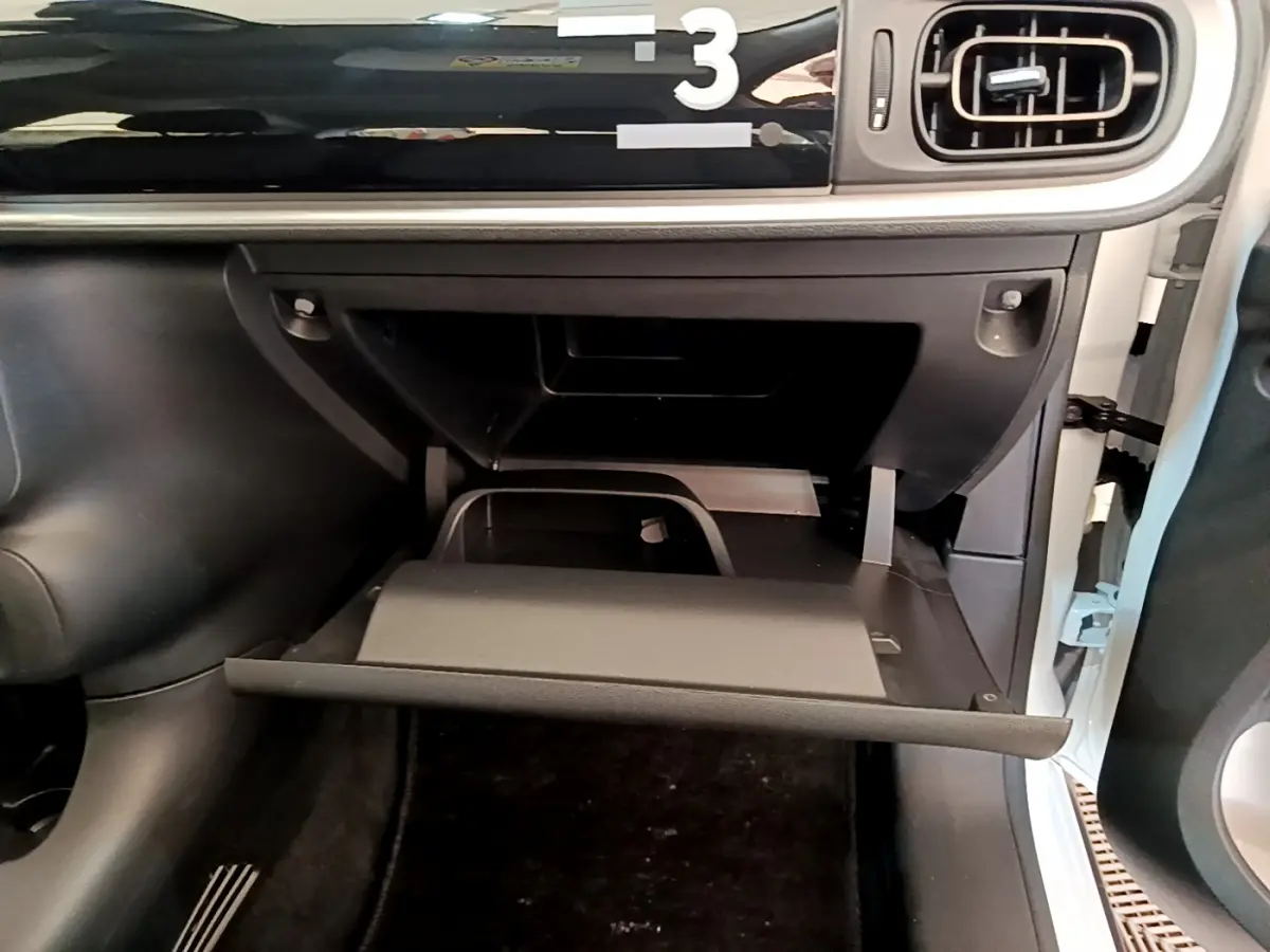 Gros plan sur la boîte à gants ouverte côté passager d'une Citroën C3 blanche, tableau de bord noir visible.