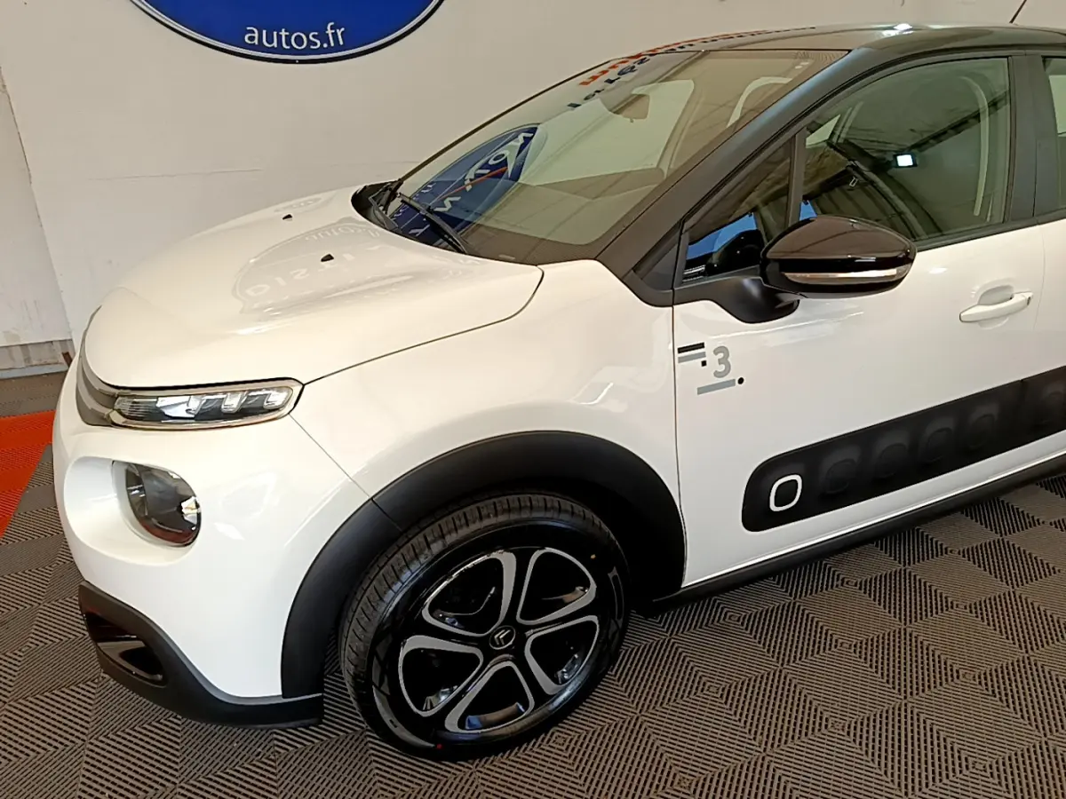 Vue 3/4 avant gauche d'une Citroën C3 blanche avec protections latérales noires et jantes stylisées noires.