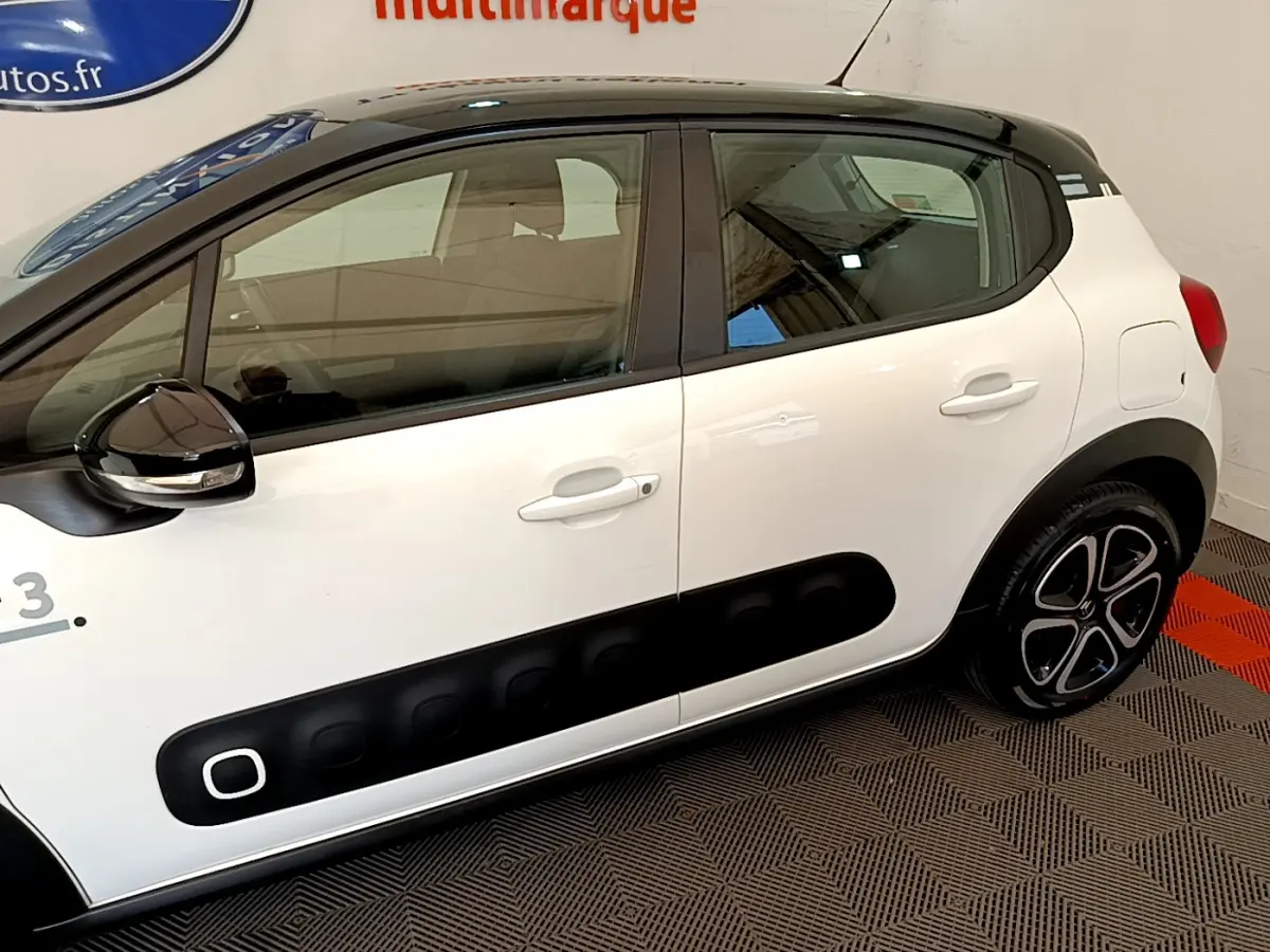 Profil côté gauche d'une Citroën C3 blanche avec toit noir et protections latérales noires distinctives.