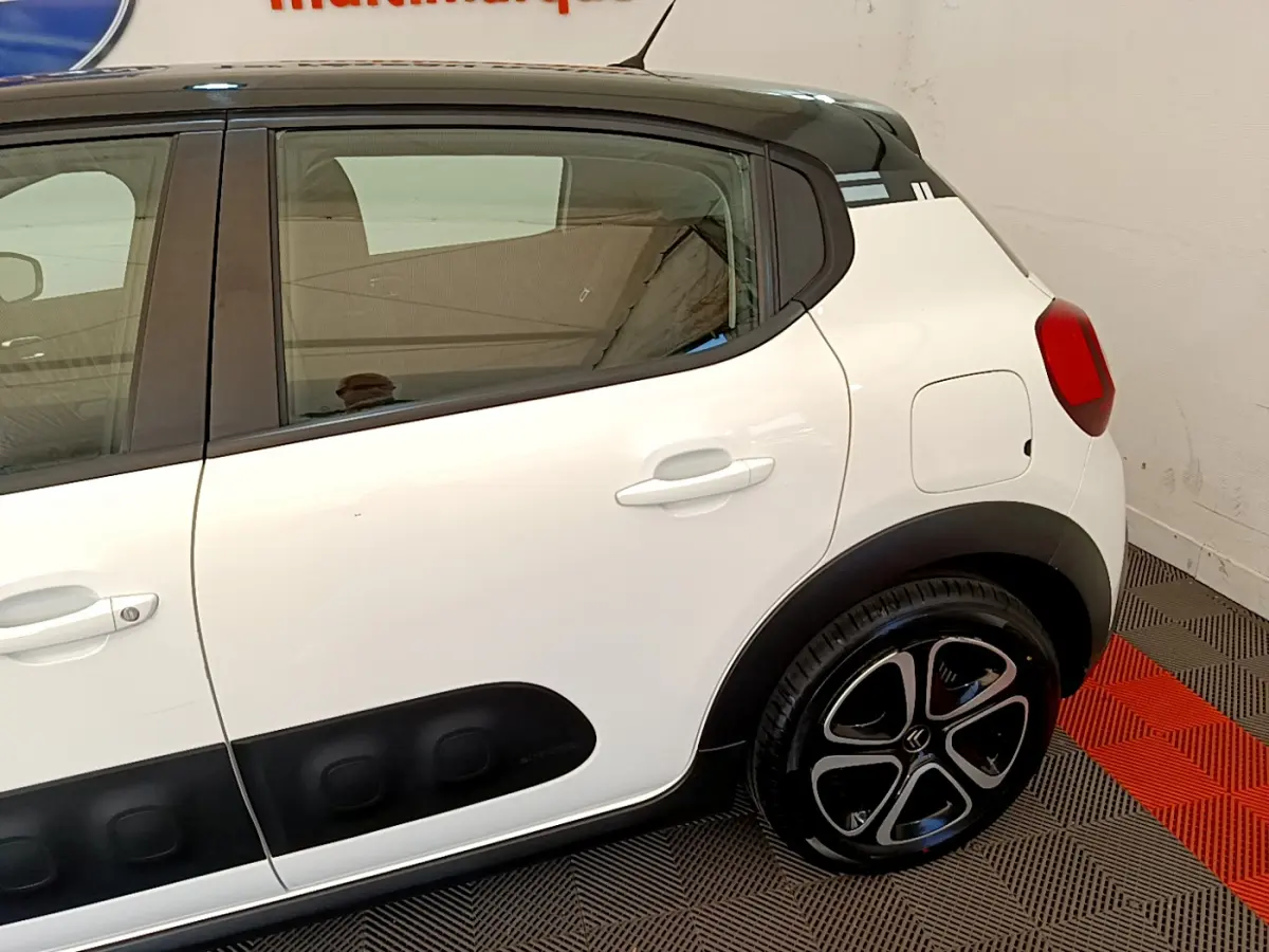 Vue latérale côté droit d'une Citroën C3 blanche avec protections noires et jantes stylisées en intérieur showroom.